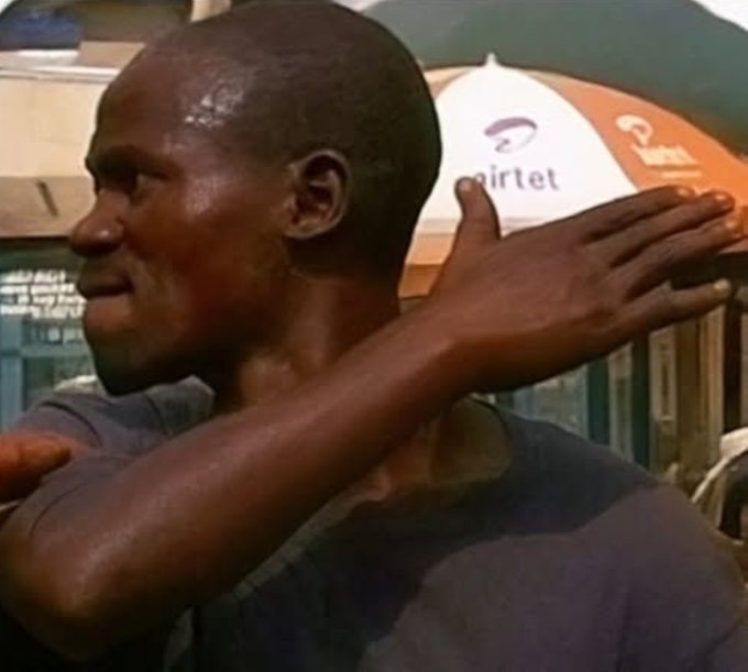 A man with a shaved head is shown in profile, wiping his face with his arm in an outdoor setting with an AirTel umbrella visible in the background.