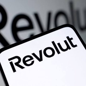 A close-up photo shows the "Revolut" logo and app icon displayed on a smartphone screen with blurred text in the background.