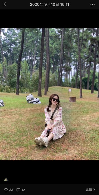 The image features an attractive young woman sitting in a grassy field near trees. She appears to be smiling as she enjoys her time outdoors, likely posing for a picture. In the accompanying caption, someone references Bitcoin, which might provide some context or background information about this digital currency.