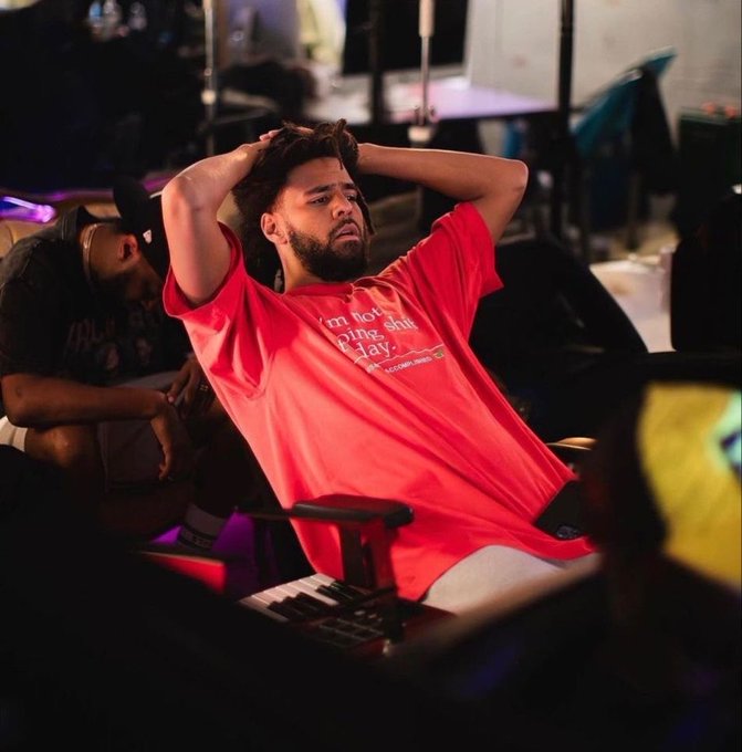 A man in a red t-shirt that reads 'I'm not boring, I'm just...' leans back in a chair with his hands on his head, looking stressed or exasperated in a studio setting.