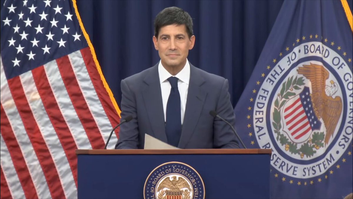 The image features a man standing behind a podium, giving a speech or addressing an audience. The man appears to be dressed formally, wearing a suit and tie. There are two flags visible in the background - one representing the United States of America with its iconic red, white, and blue colors, and another flag symbolizing the Federal Reserve Bank of the United States.

The post includes text that reads "BREAKING: PRO-#BITCOIN FED CHAIR KEVIN WARSH JUST STARTED HIS FIRST EVER FOMC PRESS CONFERENCE WE ARE WATCHING HISTORY". This suggests that the man giving the speech is a member of the Federal Reserve Bank and has just attended or is about to attend an important event, such as the Federal Open Market Committee (FOMC) press conference. The presence of these flags in the background further emphasizes the significance of this occasion.