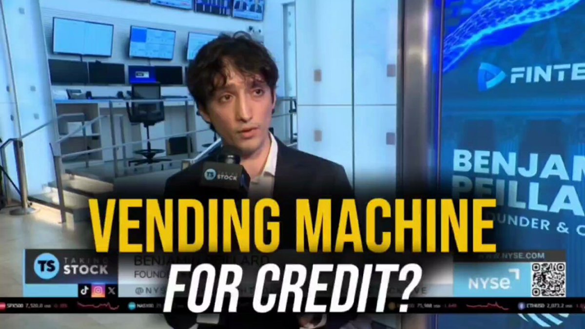 The image features a man wearing a suit standing next to a vending machine with a sign above him that says "Vending Machine For Credit?". The man appears to be talking about the vending machine as if he were explaining its purpose or discussing its features, while also referring to it as a credit vending machine. This suggests that the vending machine is designed to provide financial services and generate revenue through interest payments on loans provided by banks or other lending institutions.