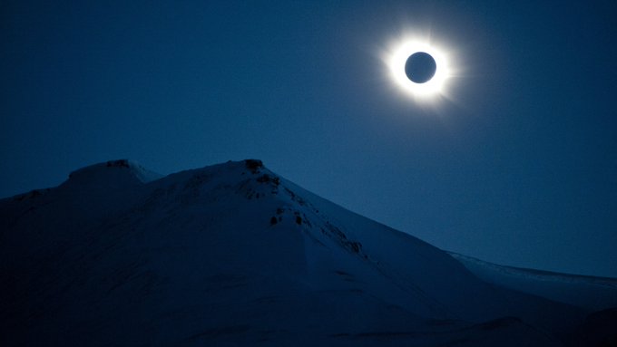 A total solar eclipse illuminates the sky above a snow-covered mountain peak, with the moon completely silhouetted against the sun's glowing corona. The image captures the dramatic celestial event shared under the caption "sole.io/totaleclipse," showcasing the awe-inspiring beauty of totality in a remote, wintry landscape.