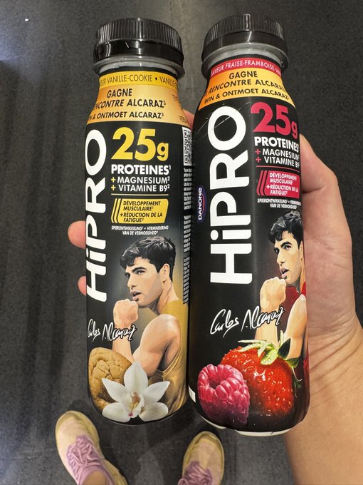 Two HiPRO protein drink bottles held in a hand — one Vanille Cookie flavor and one Fraise-Framboise (strawberry-raspberry) flavor, each featuring 25g of protein and an image of tennis player Carlos Alcaraz.
