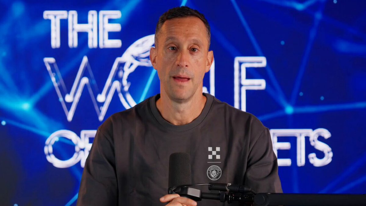 The image features a man wearing a gray sweatshirt, holding a microphone with his hands up. He appears to be speaking into the microphone or giving a presentation. The background of the image has a blue color scheme, which complements the gray tones of the man's outfit and adds depth to the scene. There is also text in the image that reads "The Wolf Of Bitcoin", possibly indicating a connection between Bitcoin and the post being discussed by the man with the microphone.