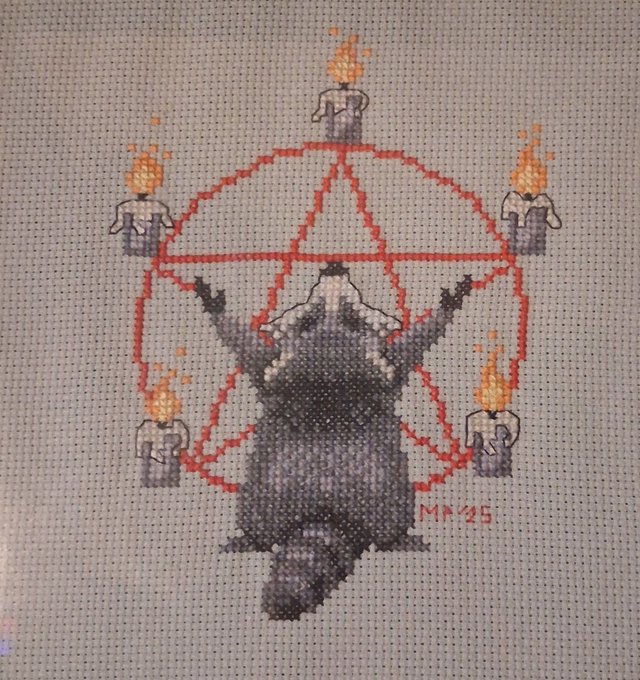 A cross-stitch artwork features a raccoon standing before a red pentagram with five flaming figures at its points, signed "MK'25" in red thread. The piece ties into the post's mention of "Coon Cabal Cult" and "$Jimothy" by depicting a "coon" (raccoon) in an occult, cult-like setting, satirically framing the meme coin as a whimsical cult initiation.