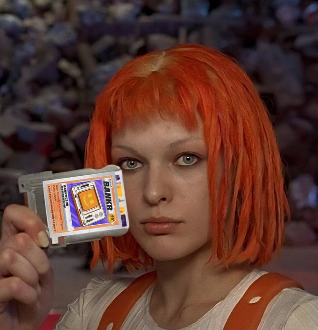 A woman with short orange hair and green eyes holds up a clear Game Boy cartridge with an orange label, looking directly at the camera against a cluttered background.