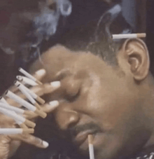 A man with multiple lit cigarettes in his mouth and hands smoking.