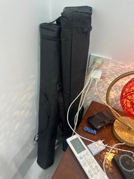 A black cylindrical carrying case stands upright next to a charging dock and remote control on a wooden table.