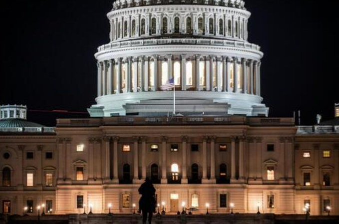 The U.S. Capitol building is illuminated at night with an American flag flying prominently, symbolizing legislative action and political progress. This image complements the post about the CLARITY Act's advancement, as the Capitol represents the venue where such regulatory legislation is debated and passed, highlighting the significance of the Major County Sheriffs of America (MCSA) withdrawing opposition to the bill.