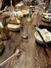 A dimly lit restaurant table set with wine glasses, a water carafe, plates, napkins, and silverware on a rustic wooden surface.