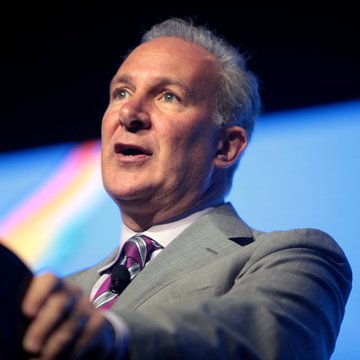 A man in a blue suit with a pink tie gestures emphatically while speaking, seemingly at a podium or panel event. The image accompanies a news post about Peter Schiff predicting Republican losses in the midterms and warning of a hostile environment for crypto and Bitcoin.