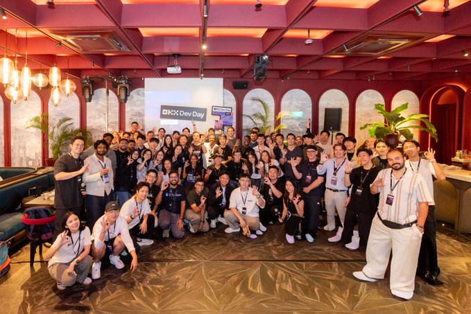 The OKX Dev Day event at Token2049 Singapore brought together a large group of attendees, as displayed on the screen behind the crowd. Team members pose together in a spacious venue, reflecting the collaborative spirit of the gathering and showcasing the active participation of the OKX Ventures team in evaluating project pitches and engaging with developers in the AI and RWA space.