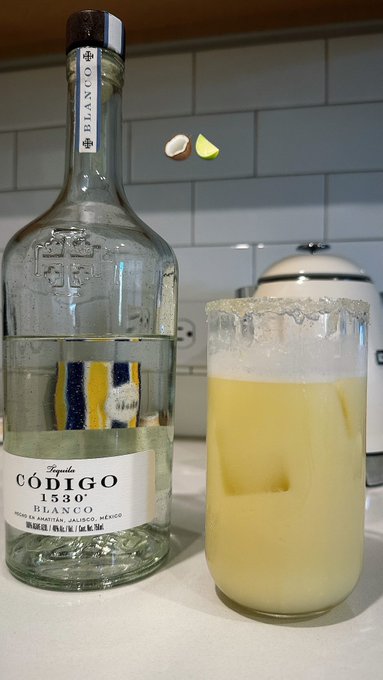 A nearly empty bottle of Código 1530 Blanco tequila sits next to a tall glass filled with a yellow cocktail featuring a salted rim, illustrating the "Time to chill" vibe with a lime wedge floating mid-air.