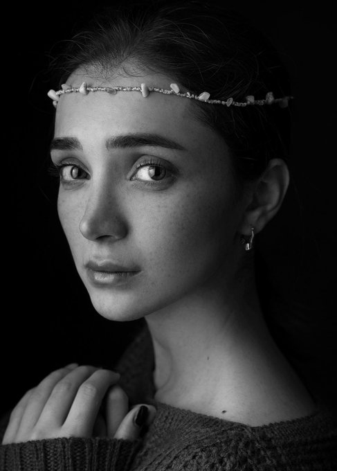 A black-and-white portrait of a young woman with freckles wearing a delicate floral headband.
