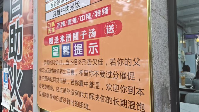 The image shows a sign for a restaurant, which has Chinese characters written on it. The sign is orange with white text that says "可以用火币每日一元买U 每天一碗木耳粉6元 用护照双号认证", and it is located on a wall. The post also mentions that the restaurant has been in business for over 50 years, which could be related to the Chinese characters or simply an interesting detail about the establishment's history.

In addition to the sign, there are two people visible in the image - one person standing near the top left corner and another person further down on the right side of the frame. The presence of these individuals suggests that this restaurant might be a popular spot for locals or tourists alike.