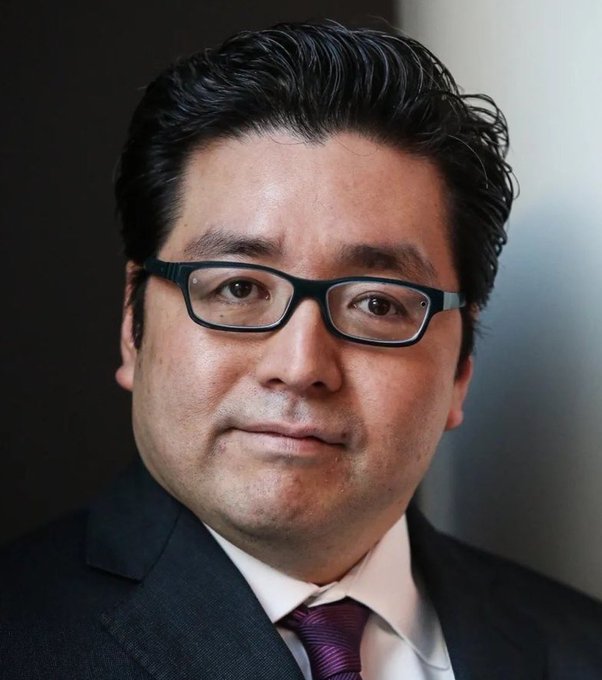 The image shows a man wearing glasses, a suit, and a tie with his head turned towards the camera, looking directly into the lens. He appears to be focused and attentive as he poses for the picture. The image also contains text that reads "Tom Lee'S Bitmine ETH investment is currently sitting at an $8.7 billion unrealized loss." This suggests that Tom Lee has some involvement in Bitmine ETH, a cryptocurrency trading platform, and it seems that his investment may have resulted in financial losses despite its value being high.
