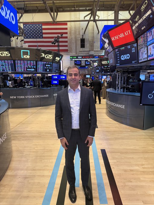 A man in a dark suit stands on the New York Stock Exchange trading floor, with the iconic "NEW YORK STOCK EXCHANGE" signage, QXO and Rosenblatt displays, and an American flag visible behind him, capturing his on-air appearance at the NYSE to discuss Robinhood Chain and enterprise adoption of the Arbitrum platform on FINTECH TV.