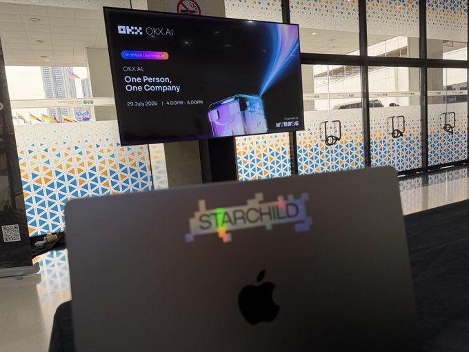 A TV screen displaying 'OKX AI: One Person, One Company' event details dated 29 July 2026, with an Apple laptop labeled 'STARCHILD TV' in the foreground.