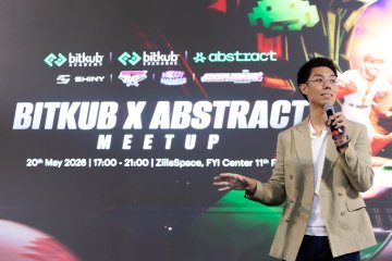 The image features a man standing at a podium, speaking into a microphone during an event. The man appears to be wearing glasses and has his hands outstretched as if he's giving a speech or presentation. Behind him, there are several posters displayed on a wall, including one that reads "I'VE BEEN WITH @AbstractChain since DAY ONE. 2024 — Abstract introduction in Thailand 2026 — Abstract announces a partnership with @BitkubOfficial". The event seems to be related to the gaming industry and could possibly be an exhibition or launch of a new game.