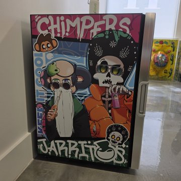 A mini-fridge with colorful graffiti-style artwork featuring cartoon characters, the word 'CHIMPERS' at the top, and 'JARBITS' at the bottom, displayed in a modern room.