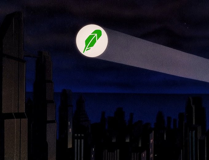 A dark, nighttime cityscape silhouette features towering skyscrapers against a deep blue sky, with a bright full moon displaying a green feather/leaf logo projecting a Batman-like searchlight beam across the scene, evoking the iconic Gotham City bat signal aesthetic associated with the $BATMANE token address shown.