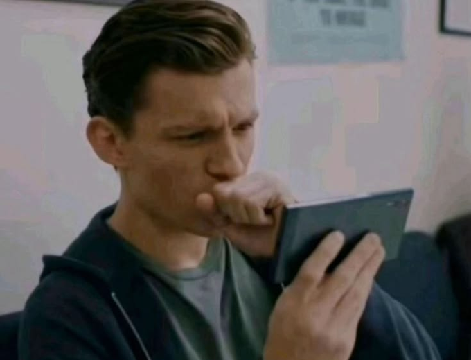 A live-action shot of a man with short brown hair wearing a dark zip-up hoodie over a t-shirt, looking intently at a tablet device while resting his fist against his mouth.