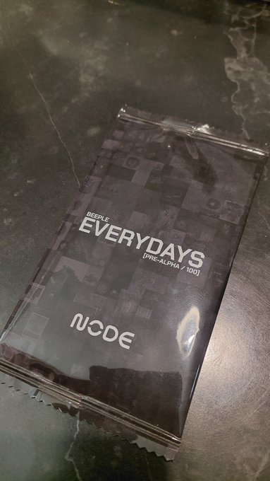 A black package of Beeple "EVERYDAYS [PRE-ALPHA #100]" NFT cards from N:CODE lying on a dark surface.