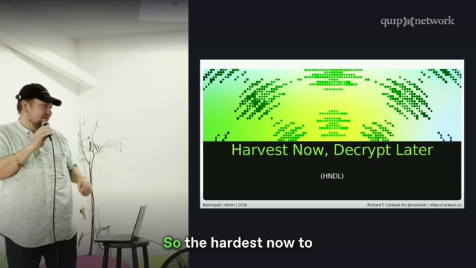 A presentation slide showing a speaker with a microphone next to a slide titled 'Harvest Now, Decrypt Later (HNDL)' from Quip Network, featuring a pixelated green graphic by Richard S. Carback.