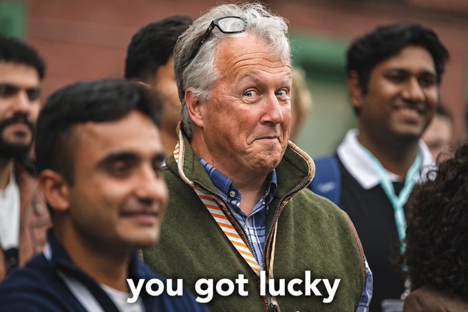 The image shows a group of people standing together, with one man wearing glasses and an old green jacket. A caption below the photo reads "you got lucky", suggesting that the man's appearance or situation might be considered luckier than others around him. The rest of the image is not described in detail but focuses on the man in the green jacket as the main subject.