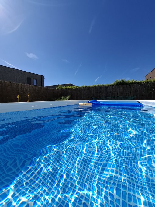 A bright blue swimming pool shimmers under a clear sky, featuring a floating pool cleaner. The serene, sun-drenched scene reflects the post's theme of stepping away from the Polymarket trading grind to recharge and reset in a peaceful setting.