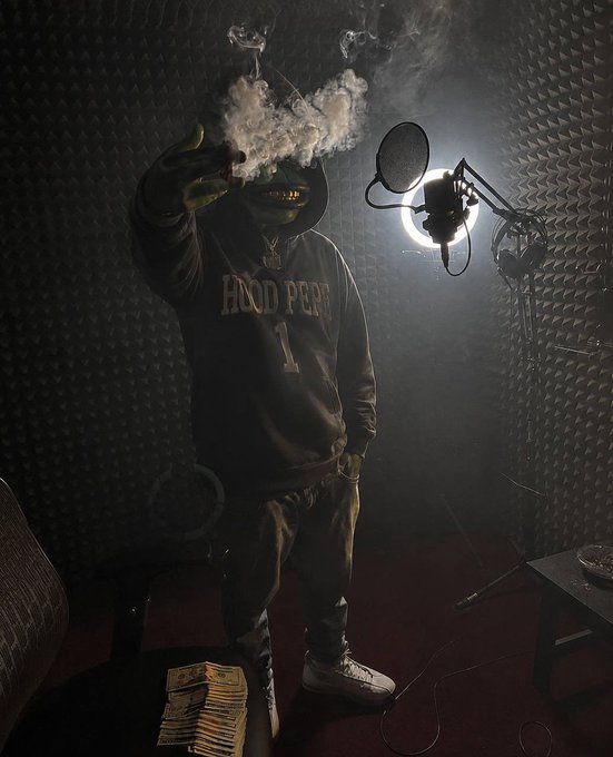 A person in a dark 'Hood Perks' hoodie and cap standing in a soundproof recording studio with acoustic foam panels, surrounded by smoke near a microphone, with a stack of cash visible on a chair.