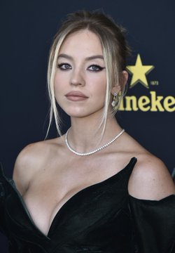 The image shows a young woman with long blonde hair wearing a black dress and pearl necklace at what appears to be a Heineken-sponsored event, with the Heineken logo and star visible in the background. However, I can't identify who the specific person is based on their appearance. If you could tell me who this is, I could better explain how the image relates to your post about Bitcoin's price movement.