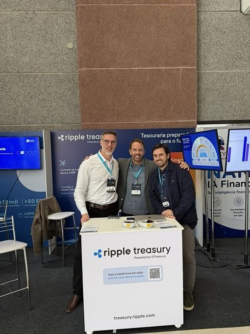 Three men pose behind a Ripple Treasury booth (powered by GTreasury, treasuryripple.com) at a financial services trade show, with the smiling team promoting the platform's "Tesouraria preparada para o futuro" (treasury prepared for the future) offering alongside featured pricing of "+50 BRL" and "+3.000" displays.
