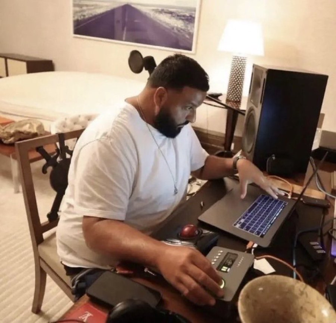A man with a beard works on a laptop while operating audio equipment in what appears to be a hotel room.