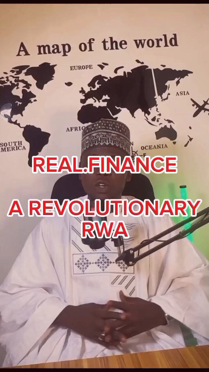 The image features a man wearing a white robe sitting at a desk with his hands folded, possibly taking part in an interview or discussion about Real Finance. The background of the image includes a map that reads "A map of the world" along with the phrase "Real finance, A revolutionary RWA". This suggests that the man is discussing real financial matters and how they can be revolutionized by implementing new ideas and strategies.