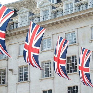 Four Union Jack flags hang outside a grand white stone building, symbolizing UK-US cooperation as agencies from both countries have agreed to conduct parallel investigations into crypto scam centers, with a joint disruption event set for London in early October.