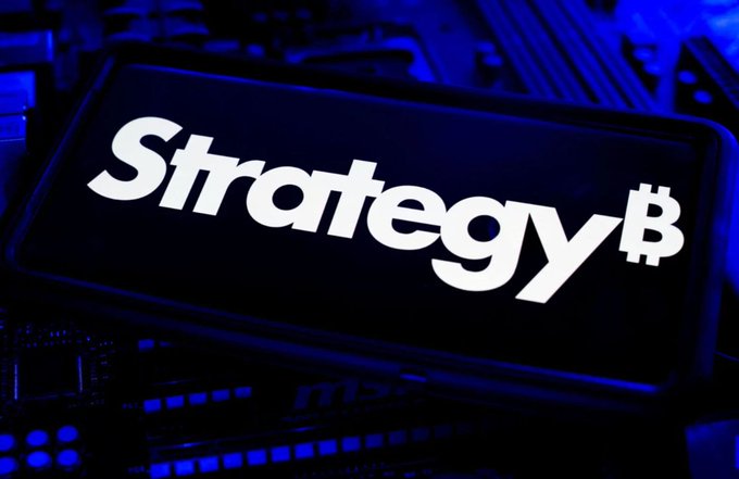 A smartphone screen displays the 'Strategy₿' logo in white text against a dark background, resting on what appears to be computer hardware illuminated by blue light.