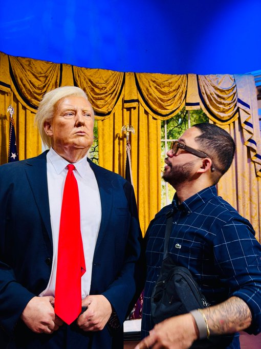 A man poses for a photo with a Donald Trump wax figure, appearing to whisper or speak closely to it, inside what looks like a museum exhibit. The caption pairs this humorous "going straight to the source" moment with a request for questions for Coach Miranda, alongside hashtags promoting trading, crypto, and Miranda Miner Profitable System content.