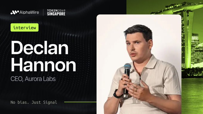 A promotional graphic from AlphaWire for TOKEN2049 Singapore featuring an interview with Declan Hannon, CEO of Aurora Labs, who is shown speaking into a microphone against a nighttime cityscape backdrop.