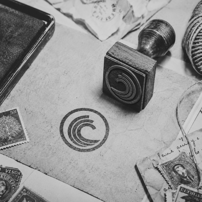 A vintage rubber stamp bearing a copyright "©" symbol rests atop scattered old U.S. postage stamps, aged letters, and a stamp pad. The faded ink impression of the © mark on the weathered paper reinforces the post's message about protecting one's creative work—"Not everyone stays, but the files always do."