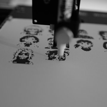 A black and white close-up image of a mechanical stamp pressing down on paper, creating pixelated character portraits.