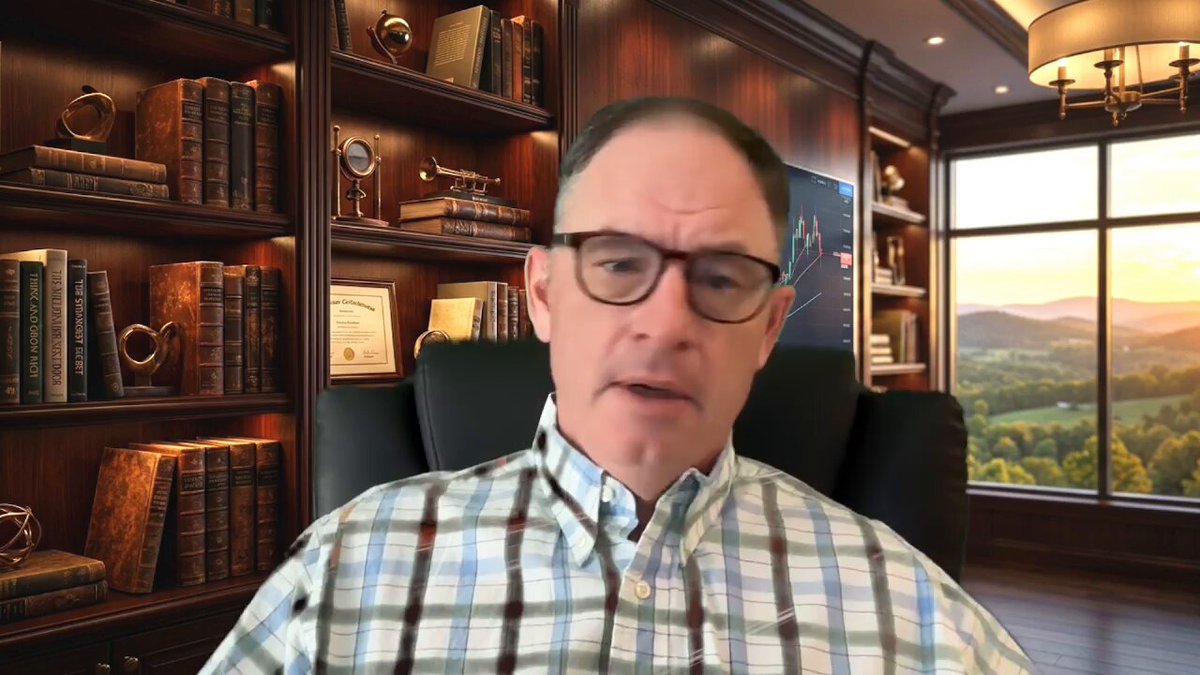 The image shows a man sitting in an office chair, wearing glasses and a plaid shirt. He appears to be giving a presentation or participating in a video call while surrounded by bookshelves filled with various books. The setting suggests that he might be discussing business matters or sharing ideas related to the books around him.