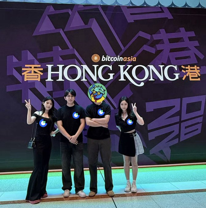 A group photo of four people posing in front of a 'Bitcoin Asia Hong Kong' backdrop, wearing matching black outfits with a logo.