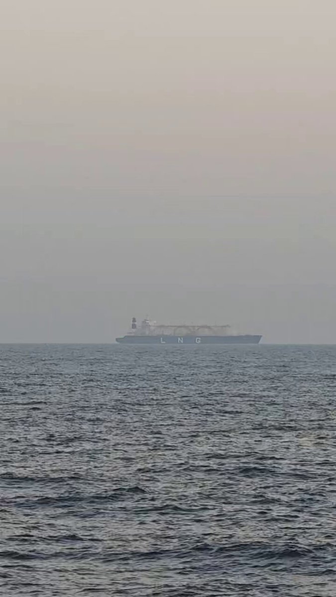 The image shows a large ship sailing across the ocean under a hazy sky. The ship appears to be a cargo vessel or a cruise liner, as indicated by its size and presence in the water. The scene captures the vastness of the ocean and the power of the ship as it sails through the waters.