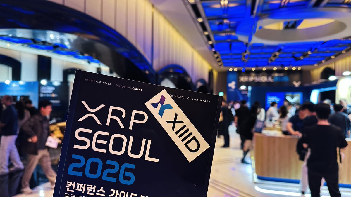A photo from the XRP Seoul 2026 cryptocurrency conference, showing a promotional sign in the foreground with attendees and booths in the background at what appears to be the Grand Hyatt venue.