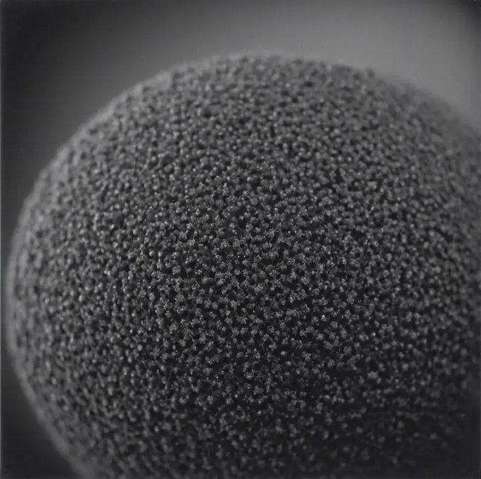 Close-up macro photograph of a textured spherical object, possibly a speaker grille or microphone foam ball, with a shallow depth of field against a blurred gray background.