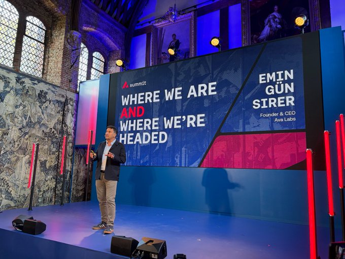 The image features an event stage with a man standing at the front speaking into a microphone, likely delivering a speech or presentation related to Summit. The stage has a blue background and red lights, creating a visually striking scene. The text "Where We Are" is prominently displayed on the stage, indicating that this is part of the Avalanche Summit series.