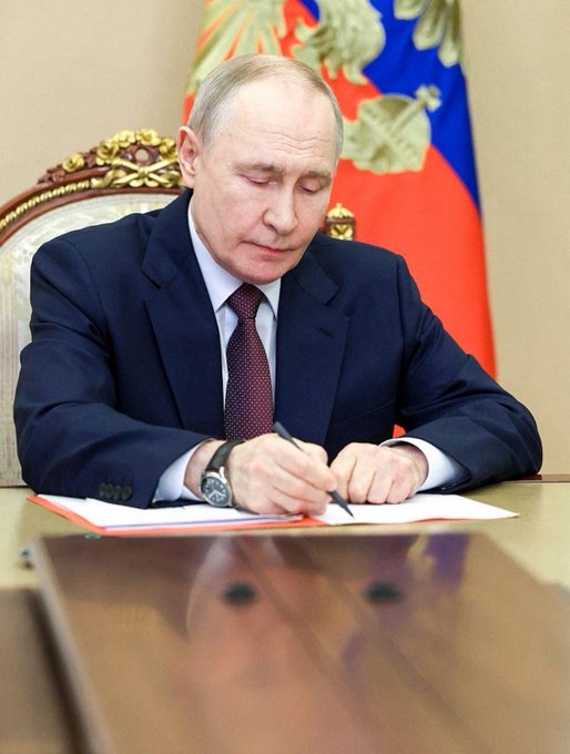 Vladimir Putin is pictured signing a document, illustrating the context of Russia establishing a regulatory framework for the cryptocurrency market.