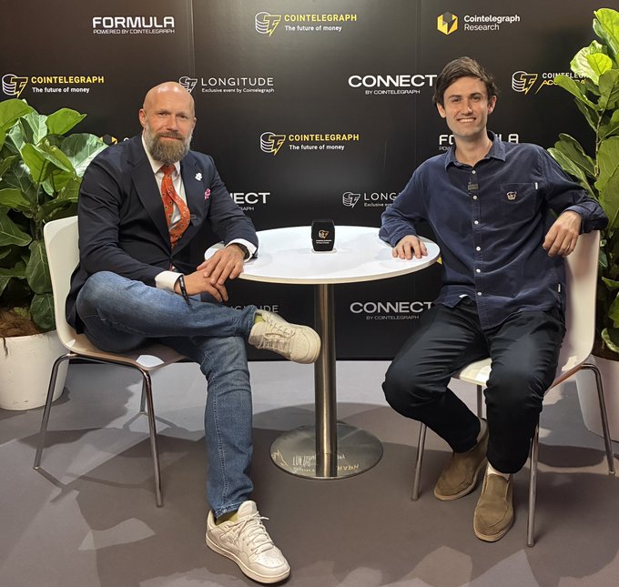 Two men seated at a Cointelegraph event with Formula, Longitude, and Connect branding in the background, appearing to be at an interview setup.